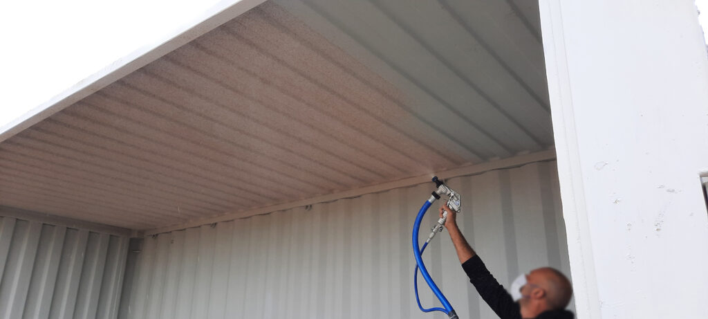 Application du Soliège sur le plafond d’un conteneur maritime à l’aide d’un pistolet à crépir.