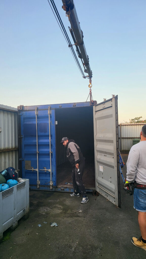 Technicien inspectant l'intérieur d'un container de stockage bleu à Montpon-Ménestérol, grue de livraison visible à l'arrière-plan.
