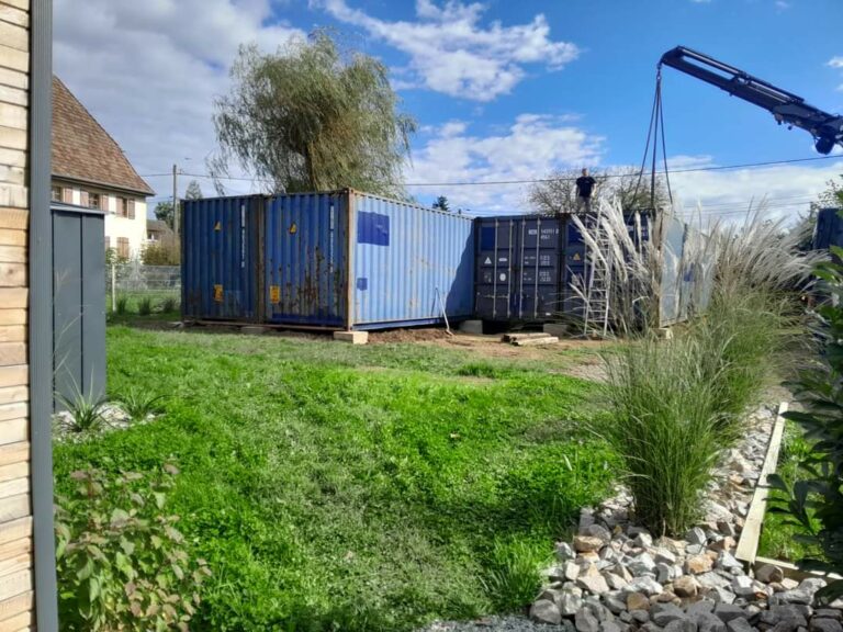 Containers maritimes bleus installés sur un terrain verdoyant pour la construction d'une maison container à Larivière, Territoire de Belfort.