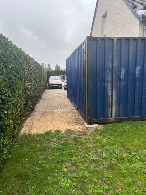 Container de stockage 20 pieds bleu utilisé comme garage par un particulier à Ambillou (37), installé à côté d’une maison et d’une haie.