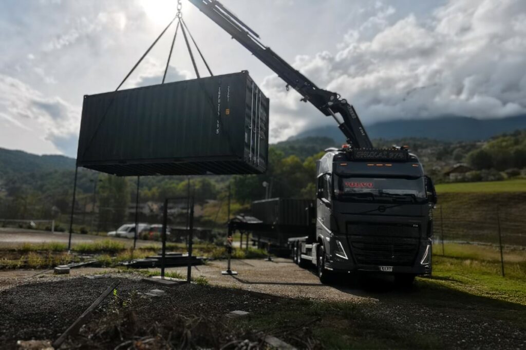 Livraison container par camion grue dans les Alpes à Marthod avec paysage montagnard savoyard en arrière-plan